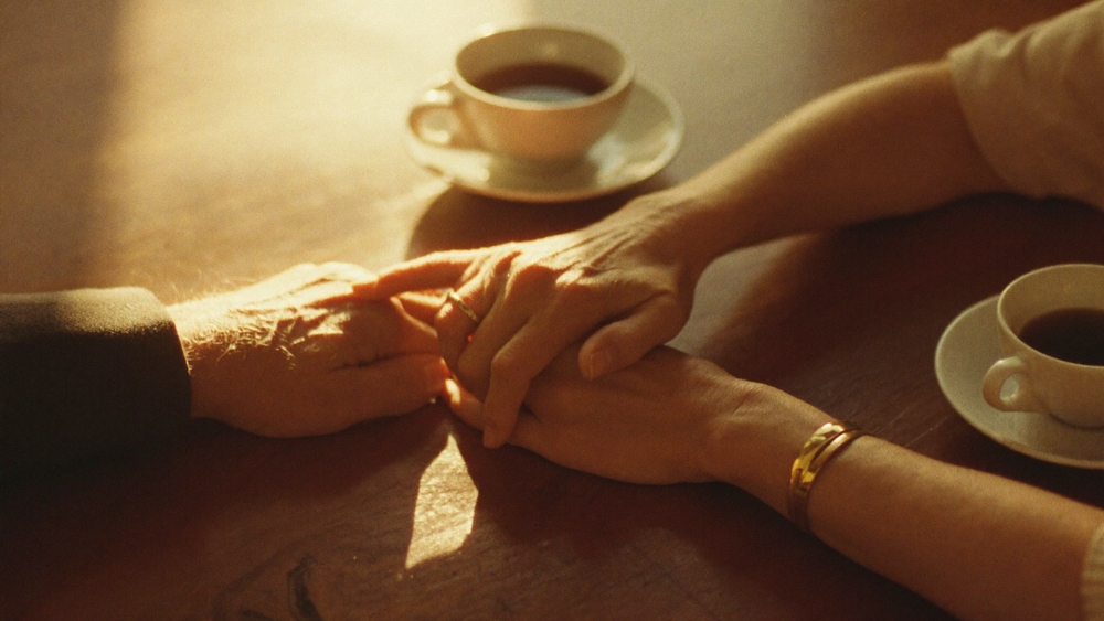 An older couple's hands together with wedding bands in warm light